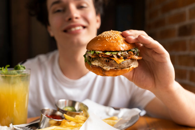 Chłopak trzymający dużego burgera, symbolizujący cheat day – zaplanowany dzień odstępstwa od diety, budzący pytania o jego wpływ na zdrowie i motywację