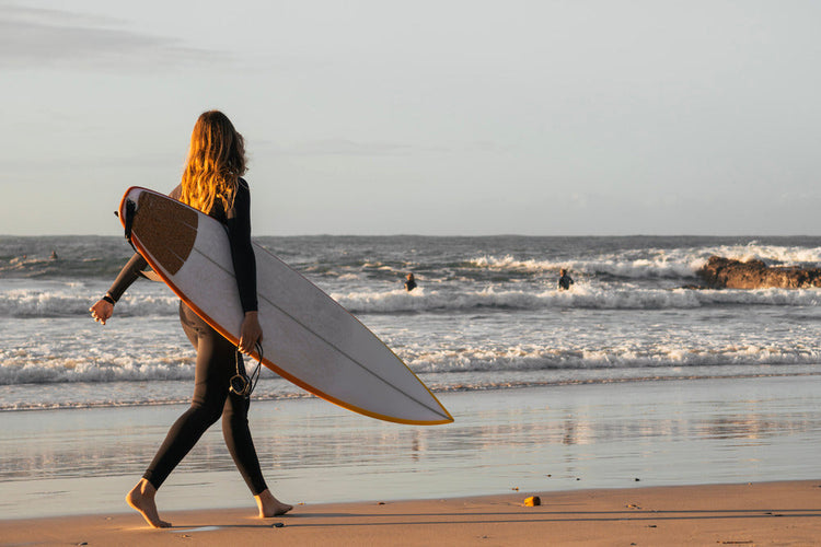 młoda surferka idzie plażą z deską o zachodzie słońca
